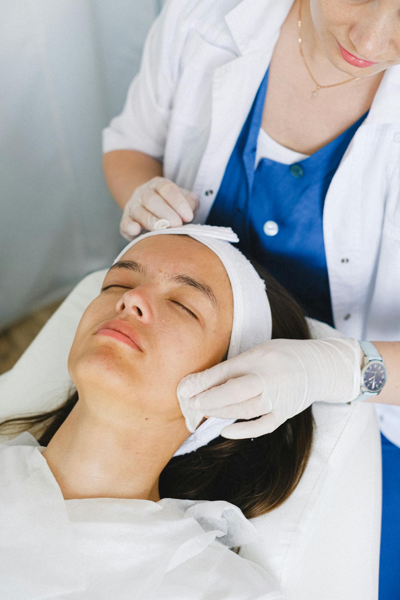From above of crop anonymous cosmetologist in medical uniform cleaning face before facial procedure in beauty clinic